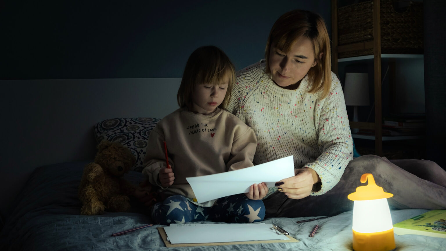 Mother and daughter sitting on bed drawing during power cut.